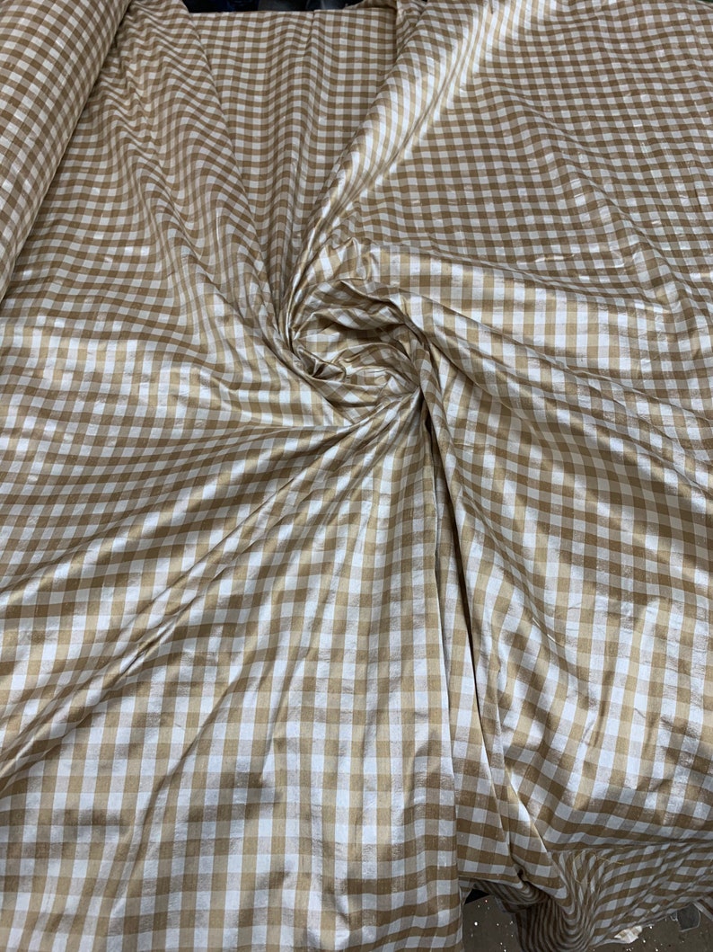May include: A brown and white gingham fabric with a subtle sheen. The fabric is folded and draped, showing the texture and pattern.