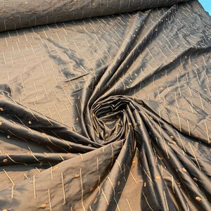 May include: A roll of brown fabric with a slight sheen. The material displays a pattern of vertical and diagonal lines, alongside small, evenly spaced dots in a lighter brown hue. The fabric is gathered in a swirl, highlighting its texture.