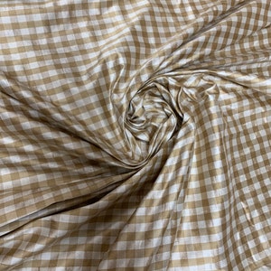 May include: A close-up of a white and gold gingham fabric. The fabric has a subtle sheen and is woven in a checkered pattern.