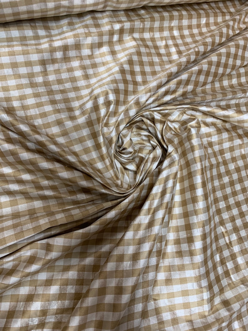 May include: A close-up of a white and gold gingham fabric. The fabric has a subtle sheen and is woven in a checkered pattern.