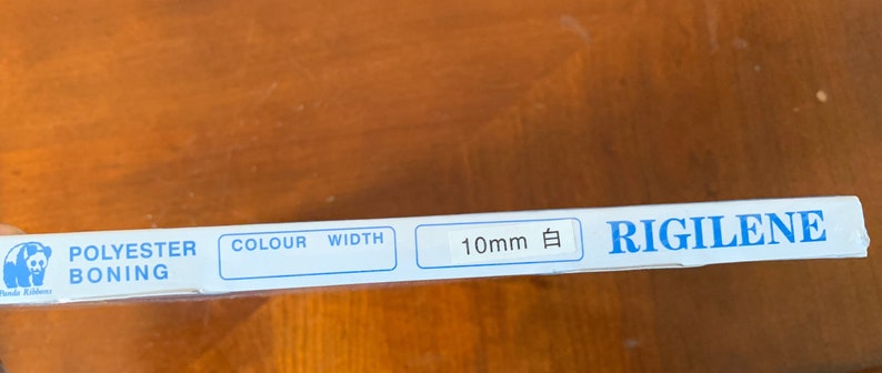 K&ouml;nnte beinhalten: Eine wei&szlig;e Verpackung mit blauem Text, der "Polyester Boning, Colour, Width, 10mm 白, RIGILENE" lautet.