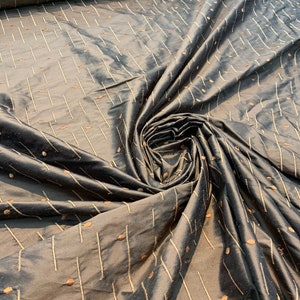 May include: Dark grey fabric with a subtle sheen, patterned with vertical lines and small dots in a lighter shade. The fabric is draped, showing folds and texture, and is likely used for clothing or home decor.