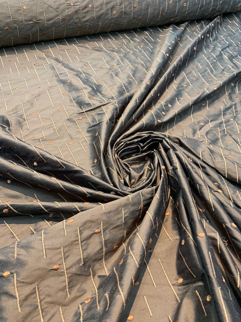 May include: Dark grey fabric with a subtle sheen, patterned with vertical lines and small dots in a lighter shade. The fabric is draped, showing folds and texture, and is likely used for clothing or home decor.