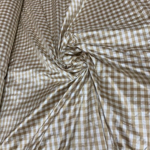 May include: A roll of brown and white gingham fabric with a subtle sheen. The fabric is folded and draped, showcasing the checkered pattern.