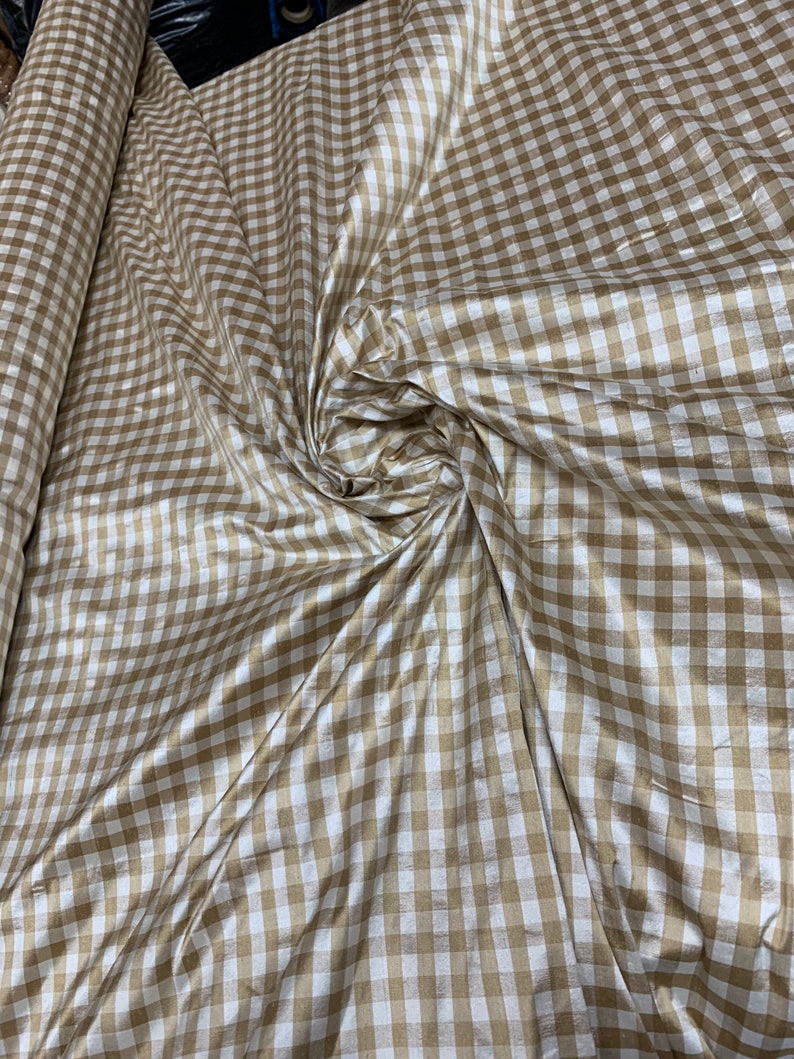 May include: A roll of brown and white gingham fabric with a subtle sheen. The fabric is folded and draped, showcasing the checkered pattern.