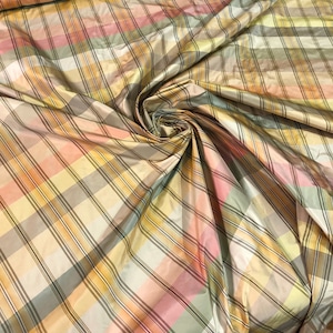 May include: A close-up of a fabric with a plaid pattern in shades of yellow, brown, pink, and green. The fabric is made of silk and has a soft, luxurious feel.