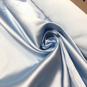 May include: Close-up of a light blue satin fabric. The fabric is draped and folded, creating a swirling pattern. The satin has a smooth, shiny texture, reflecting light and creating highlights and shadows.