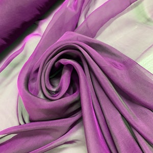 May include: Purple sheer fabric with a gradient effect, showing a darker purple hue at the bottom and a lighter purple hue at the top. The fabric is draped and folded, creating a soft and flowing look.