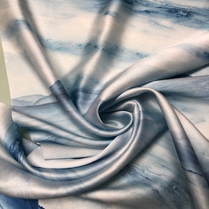 Könnte beinhalten: Ein blauer und weißer abstrakter Druck auf Seidenstoff mit weicher, fließender Textur. Der Stoff ist gefaltet und drapiert und zeigt seine luxuriöse Haptik.
