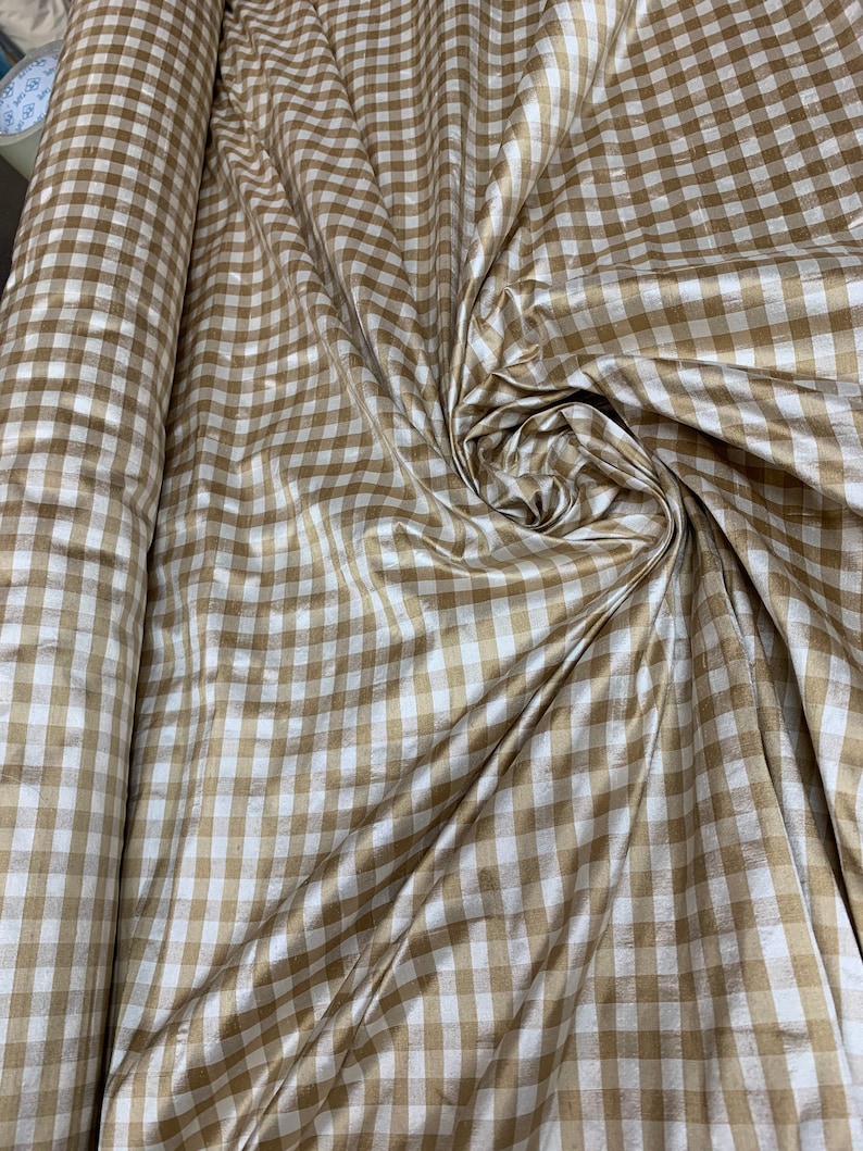 May include: A roll of white and gold gingham fabric with a subtle sheen. The fabric has a checkered pattern with a 1-inch grid.