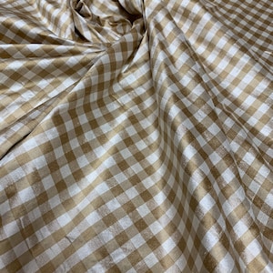 May include: A close-up of a beige and white gingham fabric with a subtle sheen. The fabric is folded and draped, showcasing its texture and pattern.