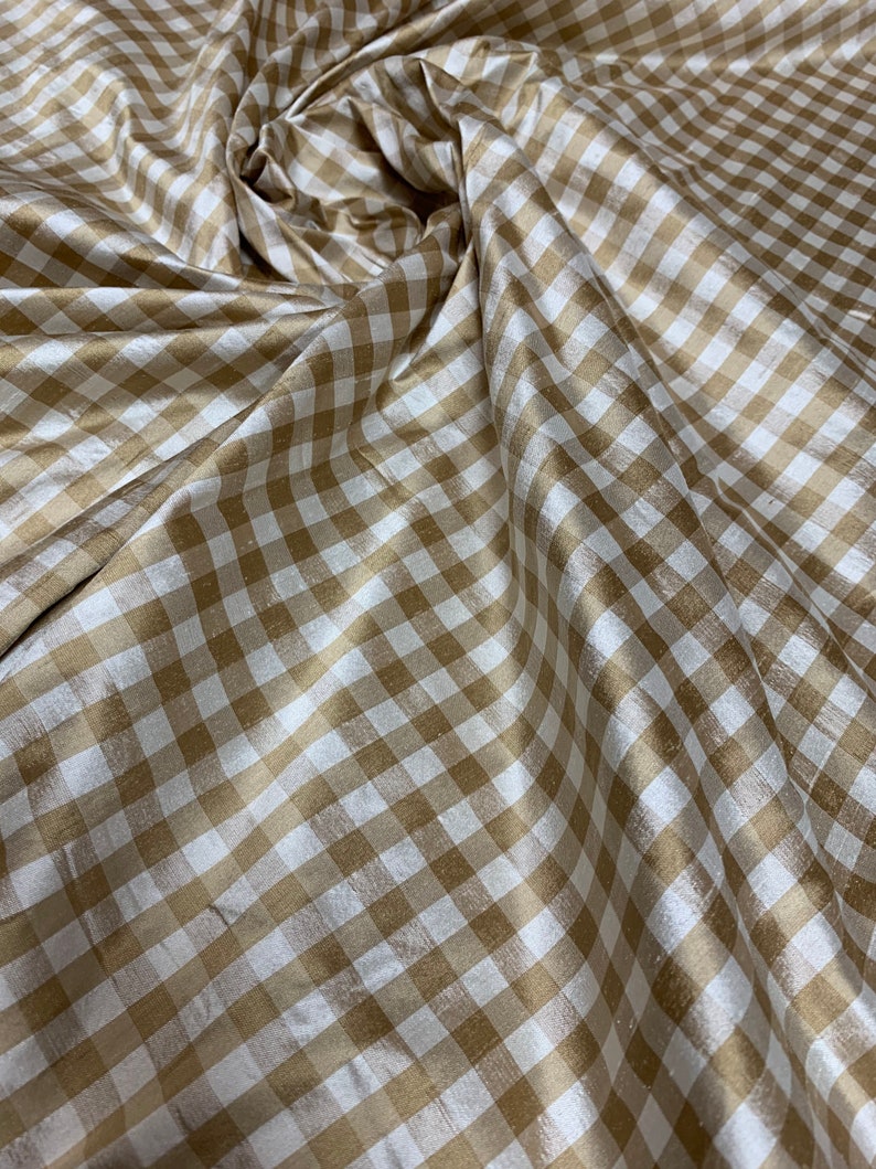 May include: A close-up of a beige and white gingham fabric with a subtle sheen. The fabric is folded and draped, showcasing its texture and pattern.