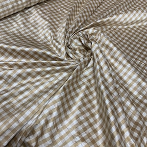 May include: A close-up of a white and gold gingham fabric. The fabric has a subtle sheen and is perfect for crafting or sewing projects.