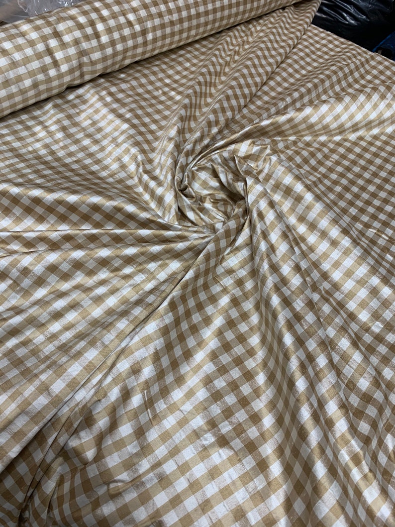 May include: A close-up of a white and gold gingham fabric. The fabric has a subtle sheen and is perfect for crafting or sewing projects.