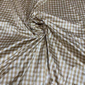 May include: A close-up of a brown and white gingham fabric. The fabric has a subtle sheen and is woven in a checkered pattern.