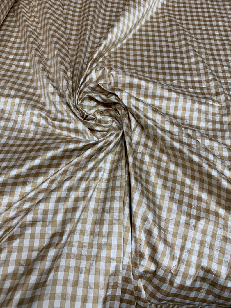 May include: A close-up of a brown and white gingham fabric. The fabric has a subtle sheen and is woven in a checkered pattern.