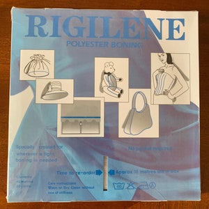 K&ouml;nnte beinhalten: Eine blaue Box mit dem Text "RIGILENE POLYESTER BONING" auf der Vorderseite. Die Box enth&auml;lt 46 Meter (50 Yards) Boning, eine Art versteifendes Material, das in der N&auml;herei und im Handwerk verwendet wird. Die Box enth&auml;lt auch Anweisungen zum Waschen und Trockenreinigen des Bonings.
