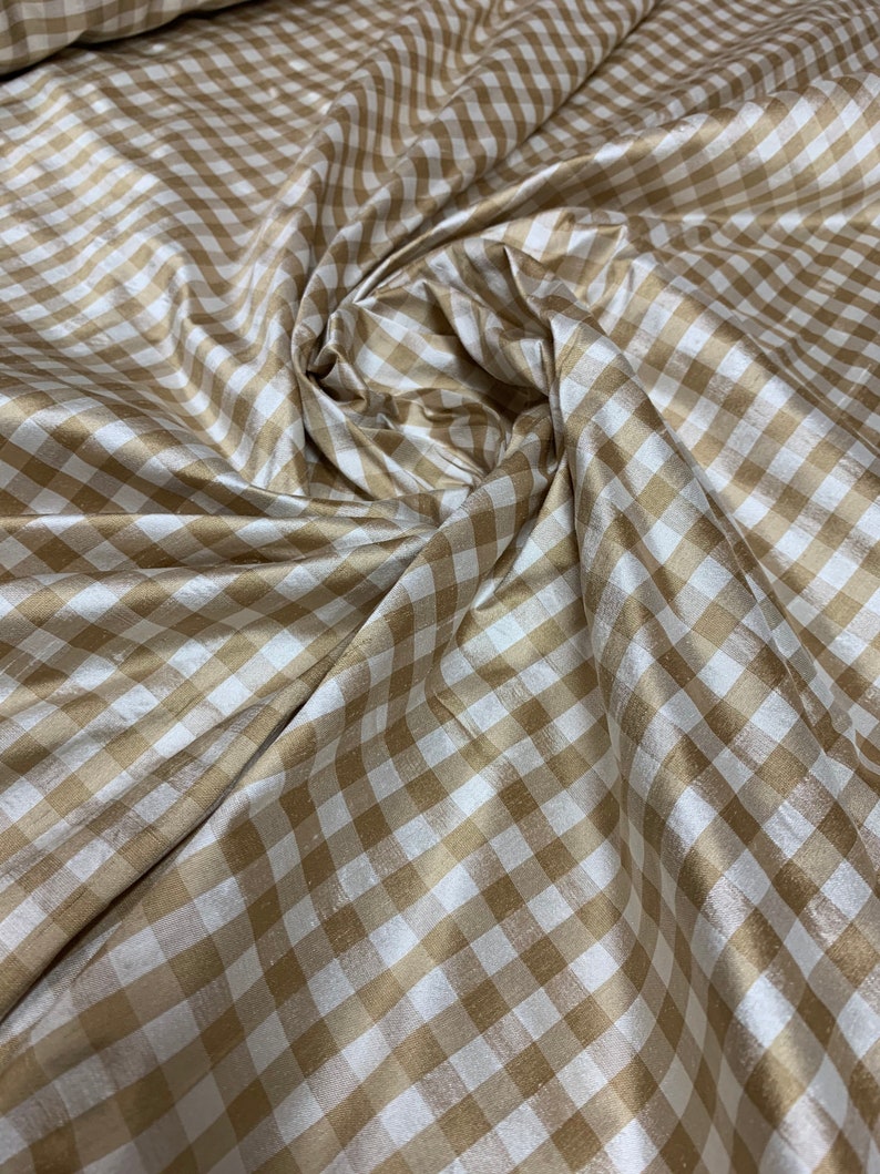 May include: A close-up of a beige and white gingham fabric. The fabric has a subtle sheen and is woven in a checkered pattern.