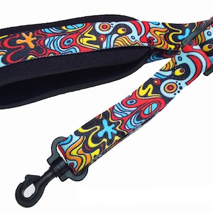 May include: A colorful guitar strap with a black and white abstract pattern. The strap has a black padded section and two black metal clasps.