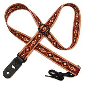 May include: A guitar strap featuring a woven fabric band with a repeating geometric pattern in shades of deep red, black, tan, and white. The strap includes black leather end tabs, a black plastic adjustment buckle, and a black nylon tie cord.