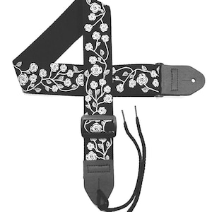 May include: Black guitar strap with a white floral rose design. The strap has a leather end and a plastic buckle for adjustment. Includes black cords for attachment to the guitar.