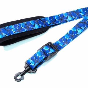 May include: A blue guitar strap with a floral pattern and black adjustable buckle. The strap has a padded section for comfort.
