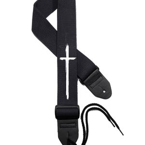May include: Black guitar strap with a white cross design. The strap has adjustable leather ends.
