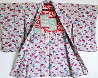 Puede incluir: Un kimono japonés tradicional con un patrón floral en tonos de rosa, azul y amarillo sobre un fondo gris claro. El kimono está abierto para revelar un forro estampado en rojo y azul con caracteres chinos.