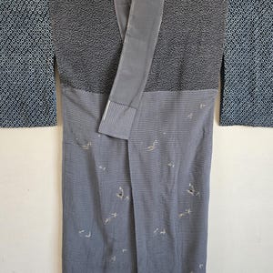 May include: A kimono featuring a two-tone design with a dark charcoal upper section displaying a fine geometric pattern and a lighter grey lower section decorated with small, scattered embroidered motifs of birds and delicate floral shapes.