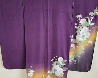 May include: A long, purple kimono with a floral design. The kimono features white flowers with green leaves and a gradient of yellow and black at the bottom. The sleeves are long and wide, and the garment is made of a smooth fabric.