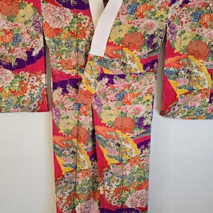 May include: A colourful floral kimono with a white collar. The kimono features a pattern of flowers in shades of pink, orange, yellow, and green. The sleeves and body are adorned with the intricate floral design, creating a visually rich garment.