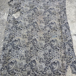 May include: A long-sleeved shirt with a floral pattern in shades of black, gray, and beige. The fabric is spread out, showing the full design of the garment. The floral print includes detailed leaves and flower shapes.