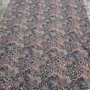 May include: A large, rectangular fabric with a repeating floral pattern. The design features stylized flowers and leaves in shades of pink, gray, and yellow against a dark background. The fabric appears to be lying flat on a concrete surface.