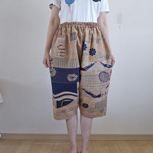 以下が含まれることがあります： 雲の模様の白いTシャツとパッチワークのクロップドパンツ。クロップドパンツは、タン色で、ネイビーブルーと白の花柄と幾何学模様です。ピンクと白の模様のサンダルと合わせています。