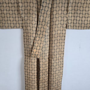 May include: A tan and black patterned kimono with a geometric design. The kimono is folded and laid flat on a white background.