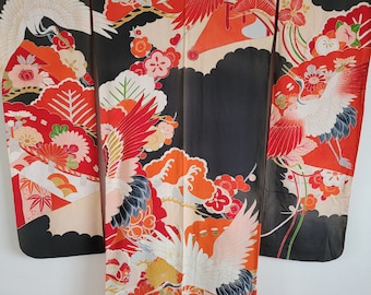 Puede incluir: Un kimono de seda negro con un estampado floral y de grúas colorido. El kimono presenta detalles en rojo, naranja, blanco y verde. Las grúas se representan en vuelo, con las alas extendidas.