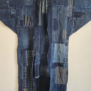Könnte beinhalten: Ein langärmeliges, indigoblau gefärbtes Kleidungsstück aus verschiedenen blauen Baumwollstoffen im Patchwork-Design. Das Stück weist eine Vielzahl von Texturen auf, darunter einfarbige, gestreifte und karierte Muster, die mit sichtbarem Garn vernäht sind.