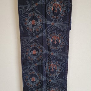 May include: A dark blue fabric with a repeating pattern of stylized floral designs in shades of blue, brown, and white. The fabric has a textured, hand-woven look.