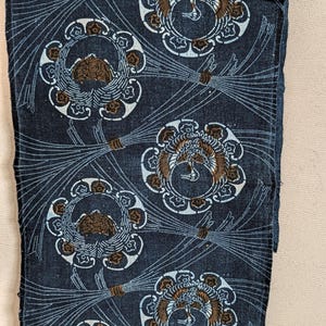 May include: A dark blue textile featuring a repeating pattern of circular motifs containing stylized birds in brown and white. The design includes thin, radiating white lines that resemble sheaves of wheat or grass, creating a structured, rhythmic layout across the fabric surface.