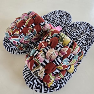 May include: A pair of fabric slippers featuring a woven, multi-colored floral pattern on the top strap in shades of red, green, and yellow. The base and sides are constructed from a dark blue and white geometric patterned fabric.