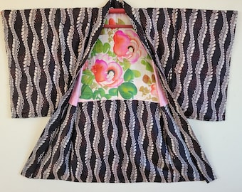 Puede incluir: Un kimono japonés con estampado en blanco y negro con un forro floral. El kimono tiene un diseño tradicional con un patrón repetitivo de hojas y enredaderas. El forro es de color rosa claro con un patrón floral en tonos de rosa, blanco y verde.