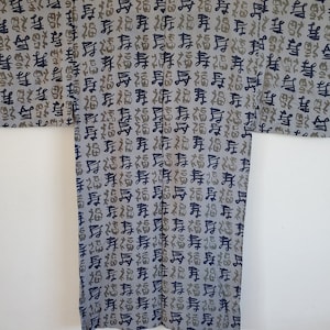 May include: A grey Japanese kimono with a black and green pattern of kanji characters. The kimono is hanging on a hanger.