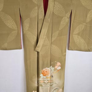 May include: An olive green vintage kimono with a floral design and a red interior. The kimono has a large floral pattern on the lower section and a geometric pattern on the upper section. The sleeves are long and wide.