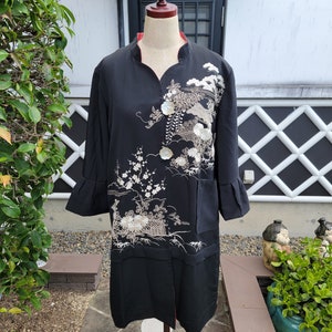 May include: A black long-sleeved jacket with white floral embroidery and pearl-like buttons. The jacket has a mandarin collar and a slightly flared hem.