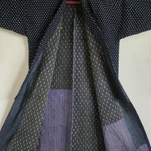 May include: A dark blue and white patterned Japanese kimono with a quilted lining. The lining is made of different fabrics, including a dark blue and white checkered fabric and a purple fabric with a subtle pattern.
