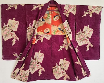 Puede incluir: Un kimono vintage en morado oscuro con un estampado floral. El kimono presenta un forro naranja vibrante y floral. Paneles color crema con ramos de flores están colocados por toda la prenda.