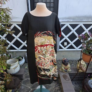 May include: Black dress with short sleeves and a round neckline. The dress features a decorative panel with a colorful floral and bird design. The dress is displayed on a mannequin.