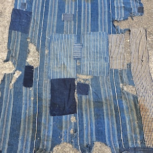 May include: A patchwork textile with a blue and white striped pattern. The textile has several patches of solid blue and checkered fabric. The fabric is distressed with visible tears and wear, giving it a vintage appearance.