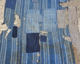 May include: A patchwork textile with a blue and white striped pattern. The textile has several patches of solid blue and checkered fabric. The fabric is distressed with visible tears and wear, giving it a vintage appearance.