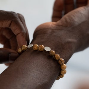 Puede incluir: Un brazalete de cuentas marrones y plateadas con un acento plateado en la muñeca de una persona.
